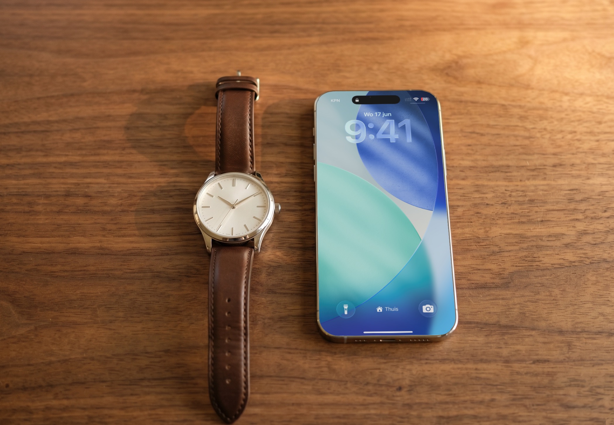 Analoog horloge met de wijzers op tien over tien, naast een iPhone met 9:41 op het scherm, op een houten tafel